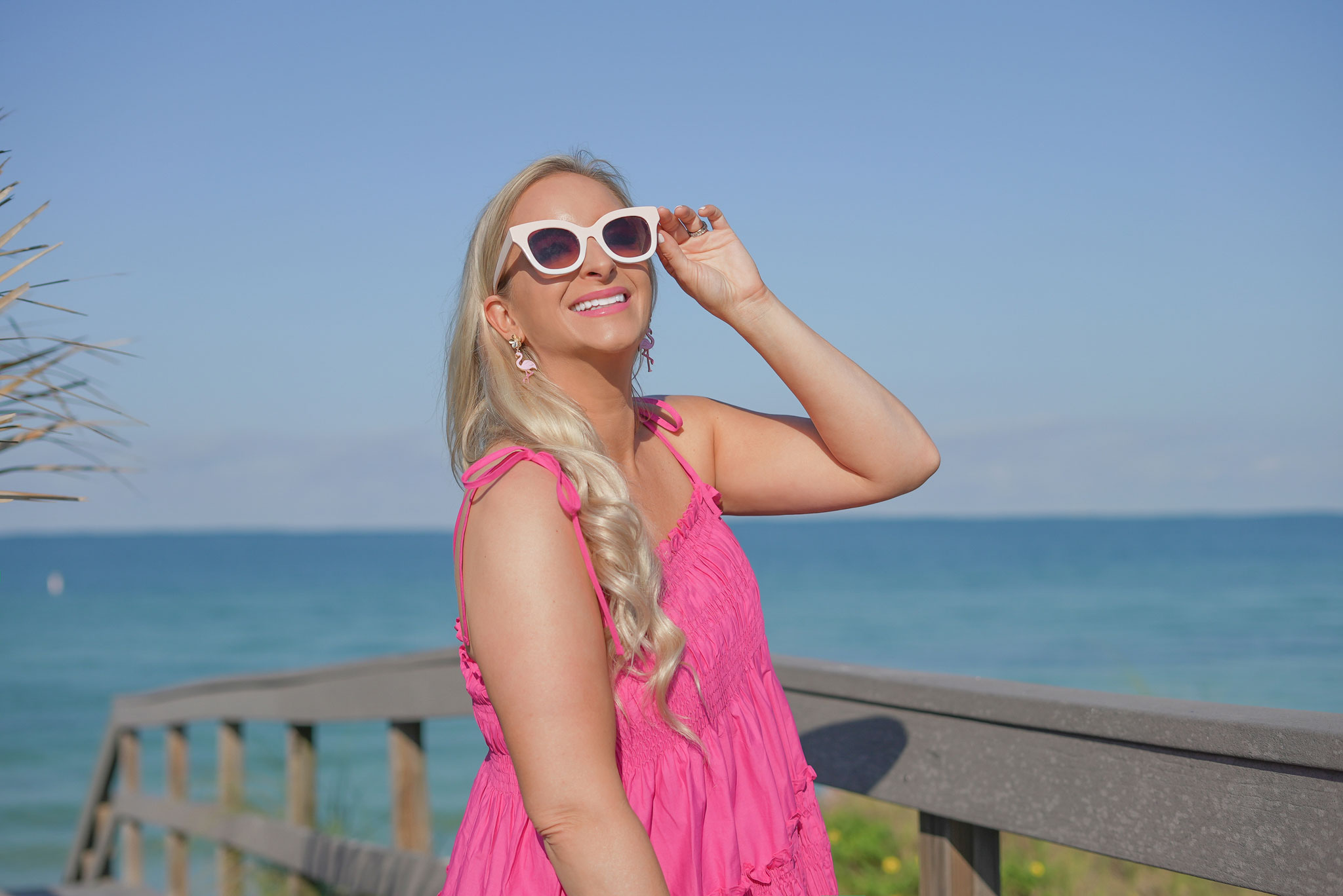 Florida Blogger, Jill DiGioia, The Lovely Flamingo wears pink flamingo earrings from her new beach earring collection along with pink sunglasses and a pink straw hat. 