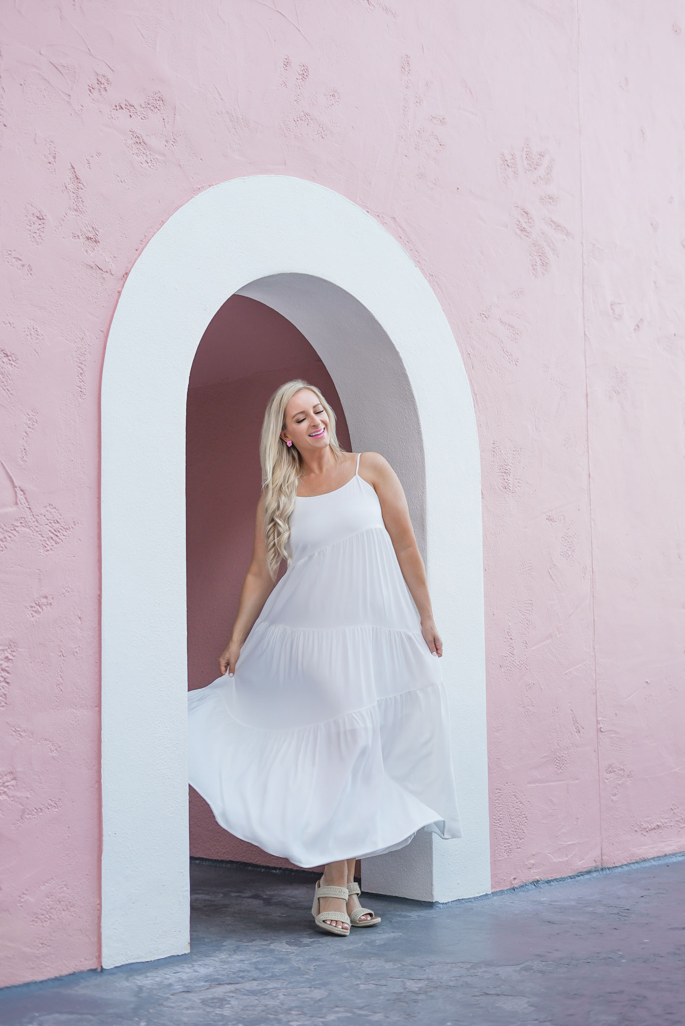 Florida Blogger, Jill DiGioia, The Lovely Flamingo wears pink hibiscus earrings from her new beach earring collection with a white maxi beach dress and standing in front of the Don Cesar Hotel on St. Pete Beach.
