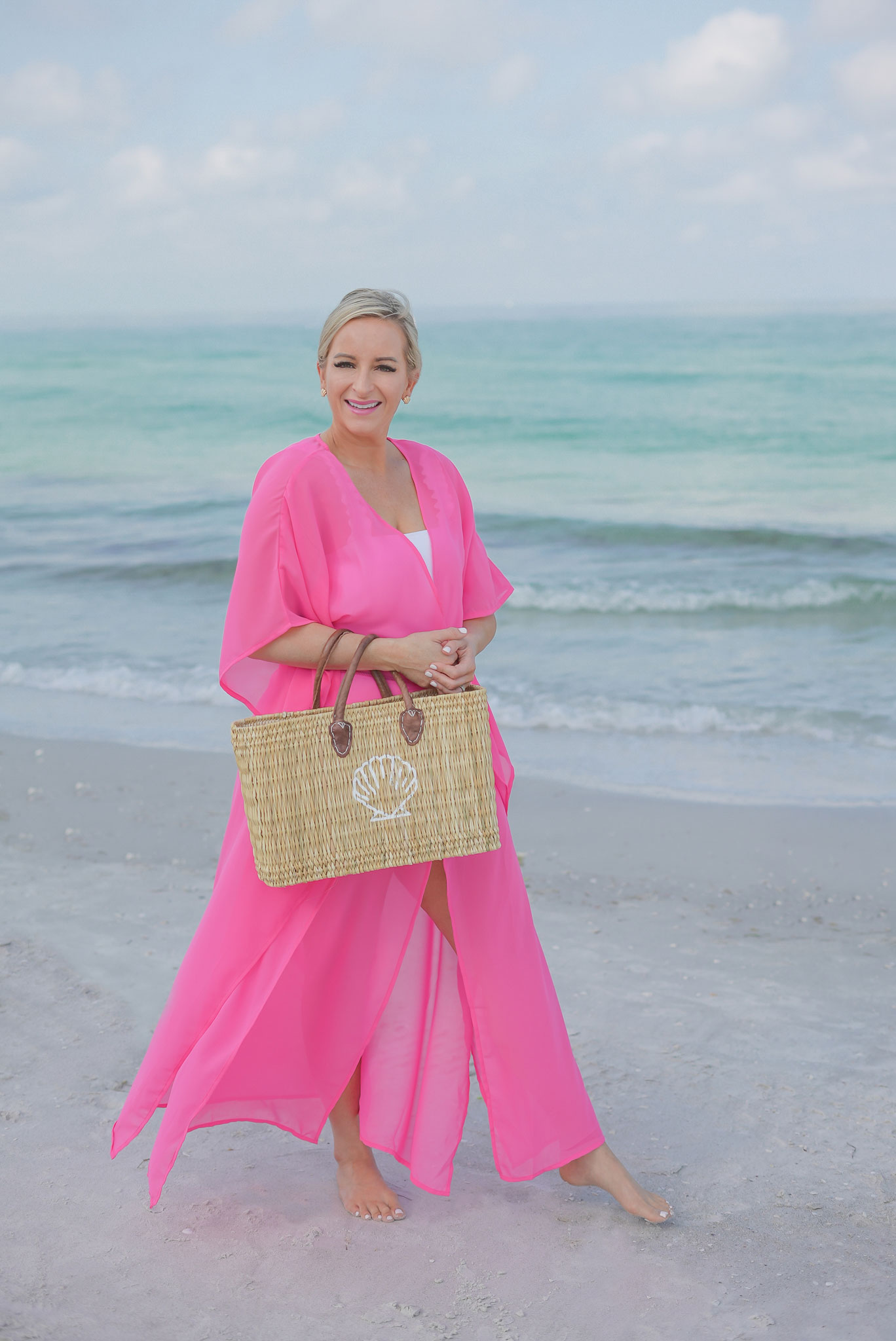 Florida Blogger, Jill DiGioia, The Lovely Flamingo wears gold shell earrings from her new beach earring collection with a hot pink beach coverup maxi kimono over a white ruffle one piece and walking on St. Pete Beach.