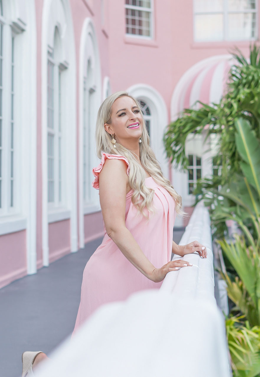 Florida Blogger, Jill DiGioia, The Lovely Flamingo wears gold shell earrings with pearl drop from her new beach earring collection with a pink midi beach dress standing in front of the Don Cesar on St. Pete Beach.