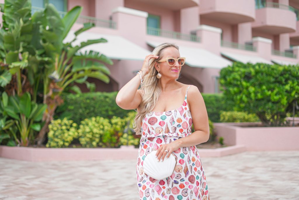 A woman in floral dress holding a white purse.