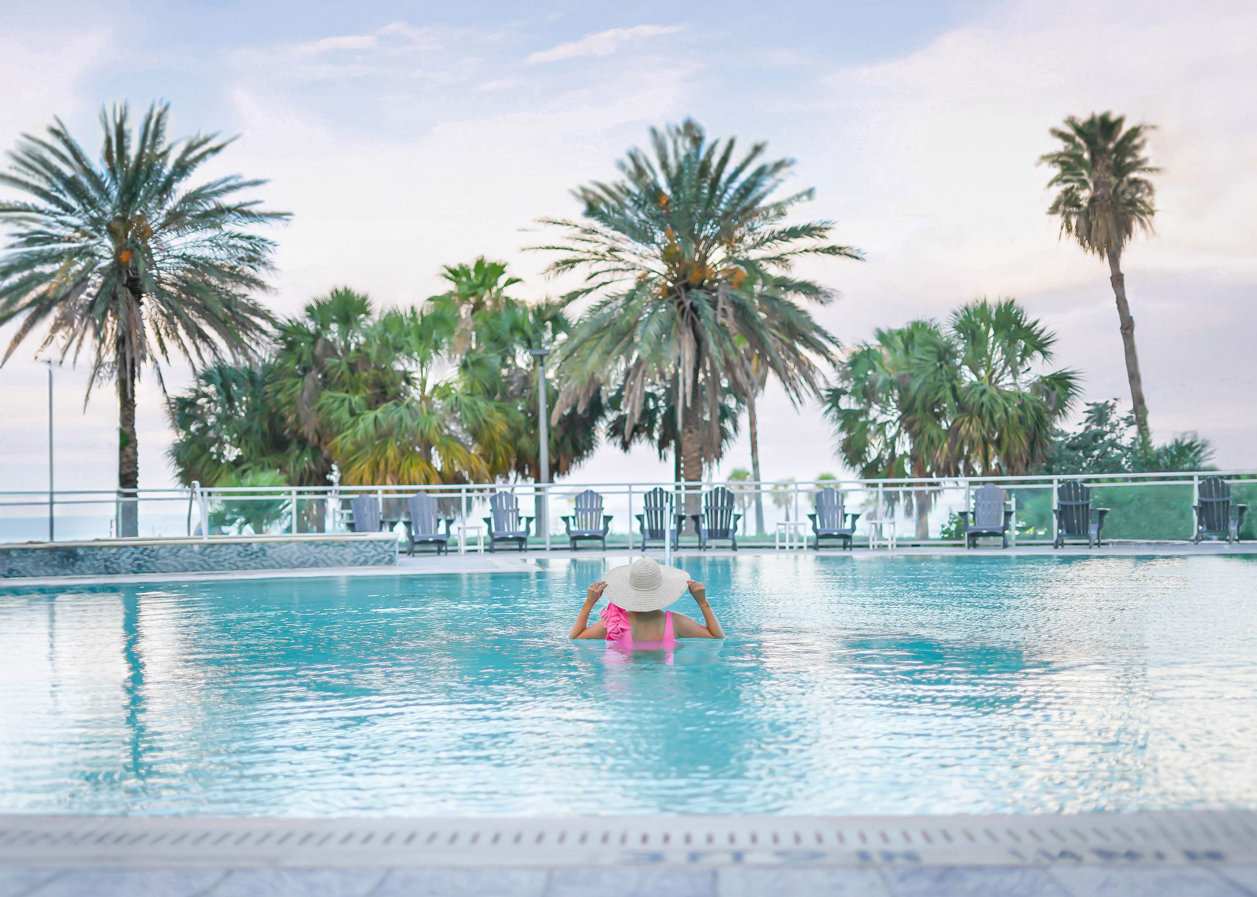 Florida Blogger, The Lovely Flamingo stands in a pink ruffle one piece swimsuit in the pool overlooking the beach at the Wyndham Grand Clearwater Beach.