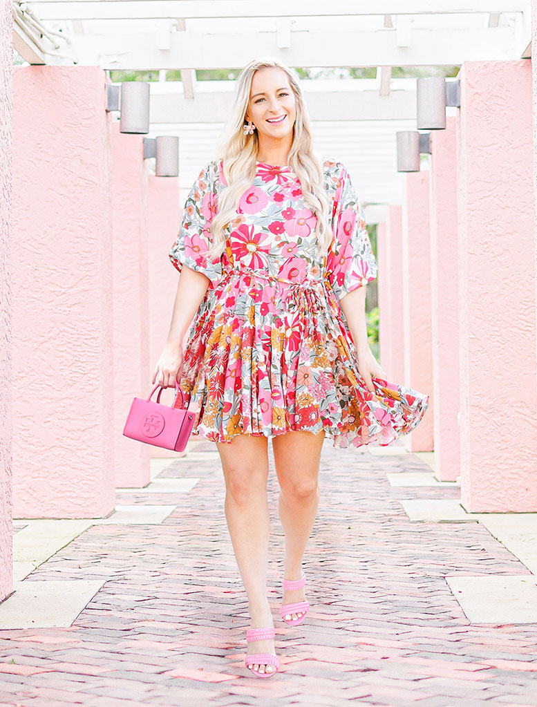 Florida Blogger Jill DiGioia wears a pink floral dress paired with pink heels, floral earrings, and a pink mini tote bag.